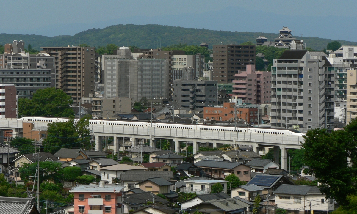 Kumamoto City actual view — Kyushu Shinkansen passing through downtown with Kumamoto Castle visible in distance